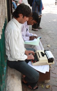 Man at typewriter with a long back, not slouching, sitting on low wall